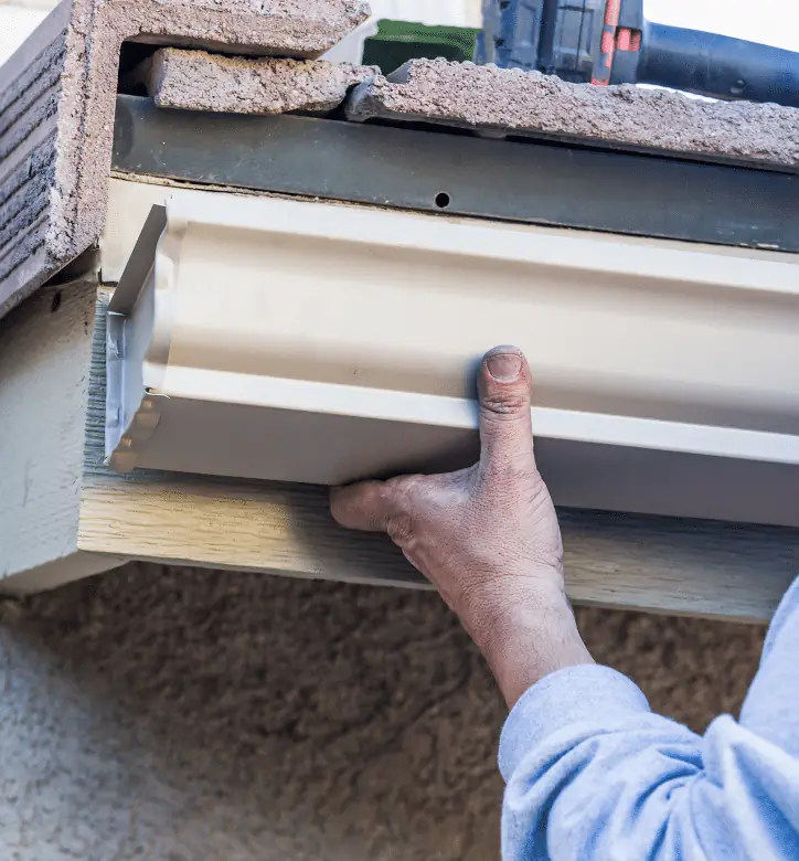 Installer pressing a new beige aluminum gutter into place under a tile roof
