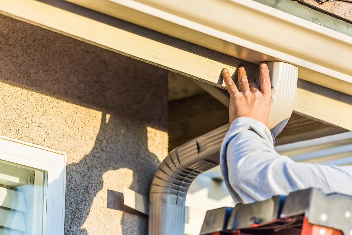 a worker installing a rain gutter system on a house. This system is crucial for home maintenance and protection