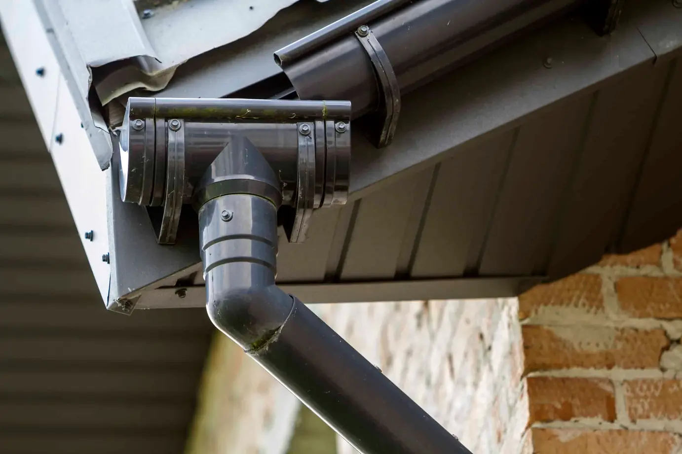 Gray downspout connector on a gutter under a metal roof