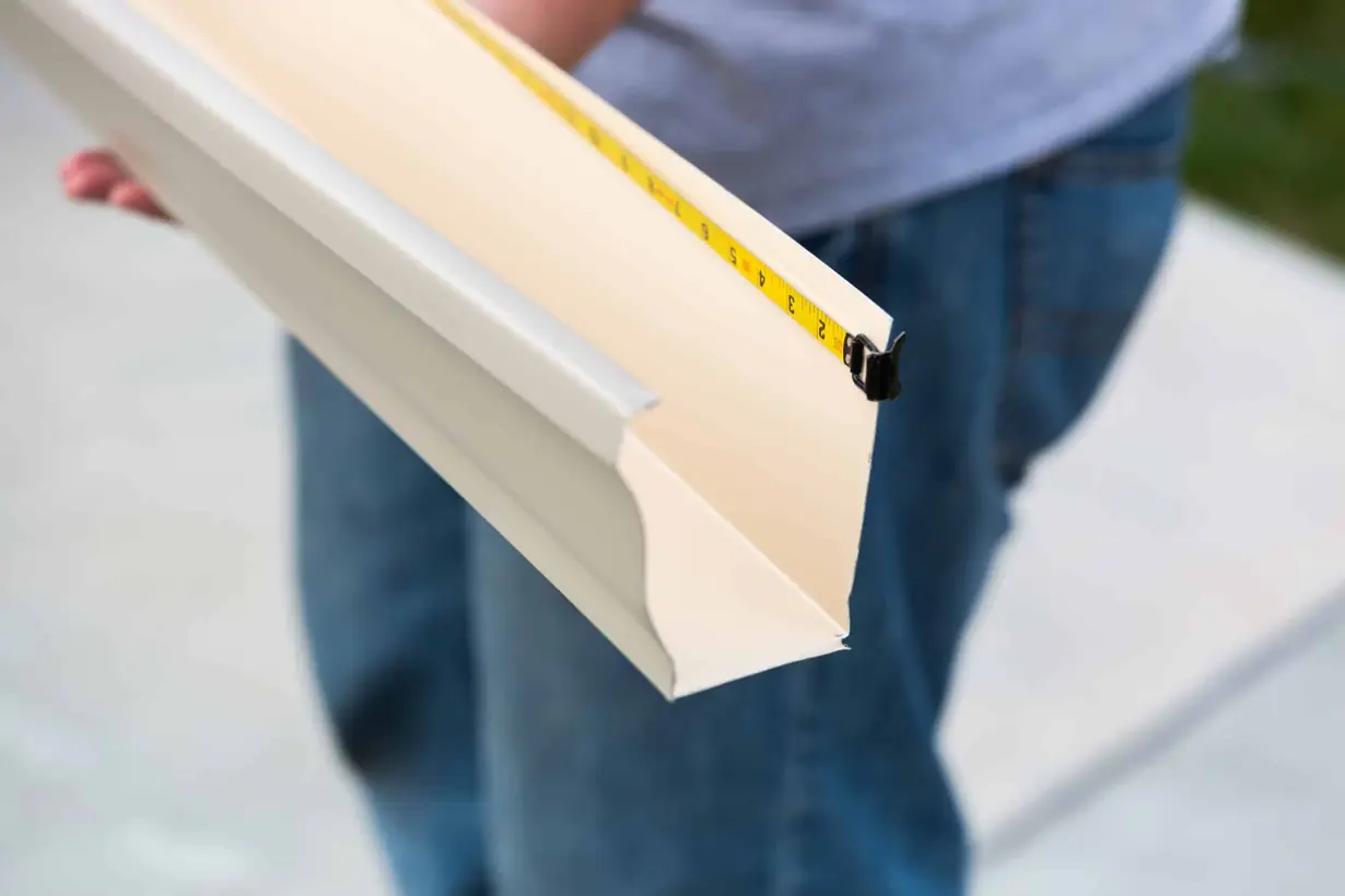 an aluminum K-style rain gutter being measured with a tape measure