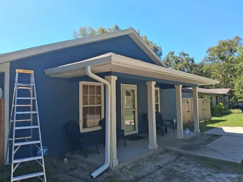 Blue home with new white gutters and a downspout at the porch, ladder in front