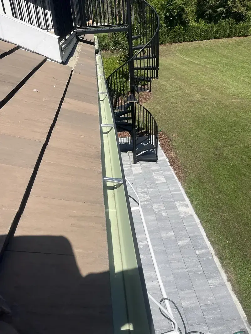 Brown gutter running along a roof above a paver walkway
