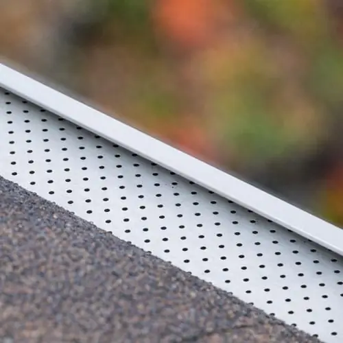 Perforated aluminum gutter guard along a shingle roof