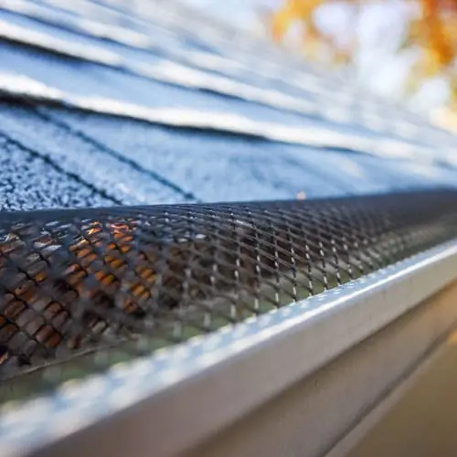 Close-up of a metal mesh gutter guard covering a gutter below a shingle roof
