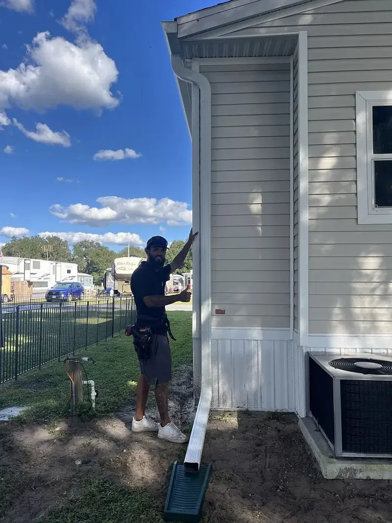 Installer attaching a white downspout to a home with vinyl siding