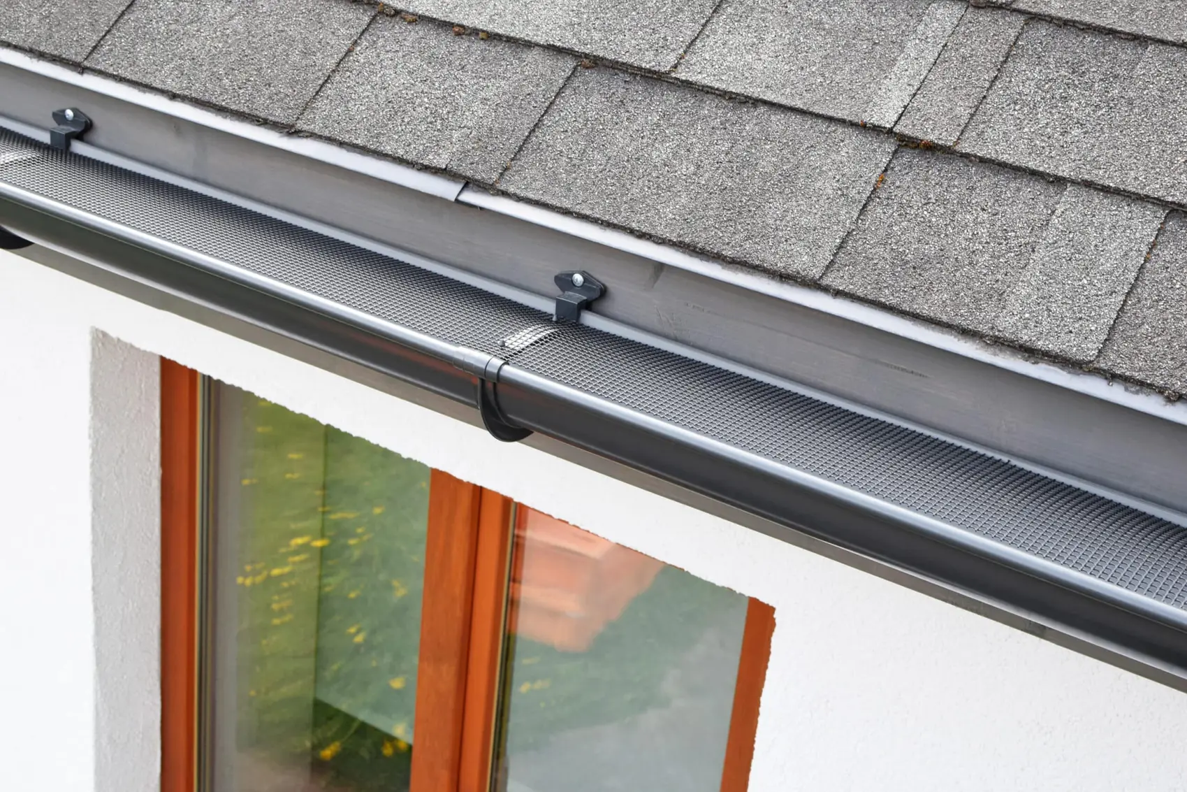 Dark gutter with a micro-mesh guard below a shingle roof