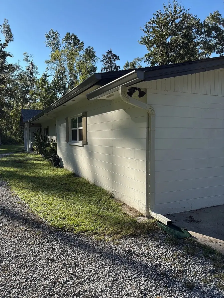 White gutter along the roof edge of a block home among pine trees