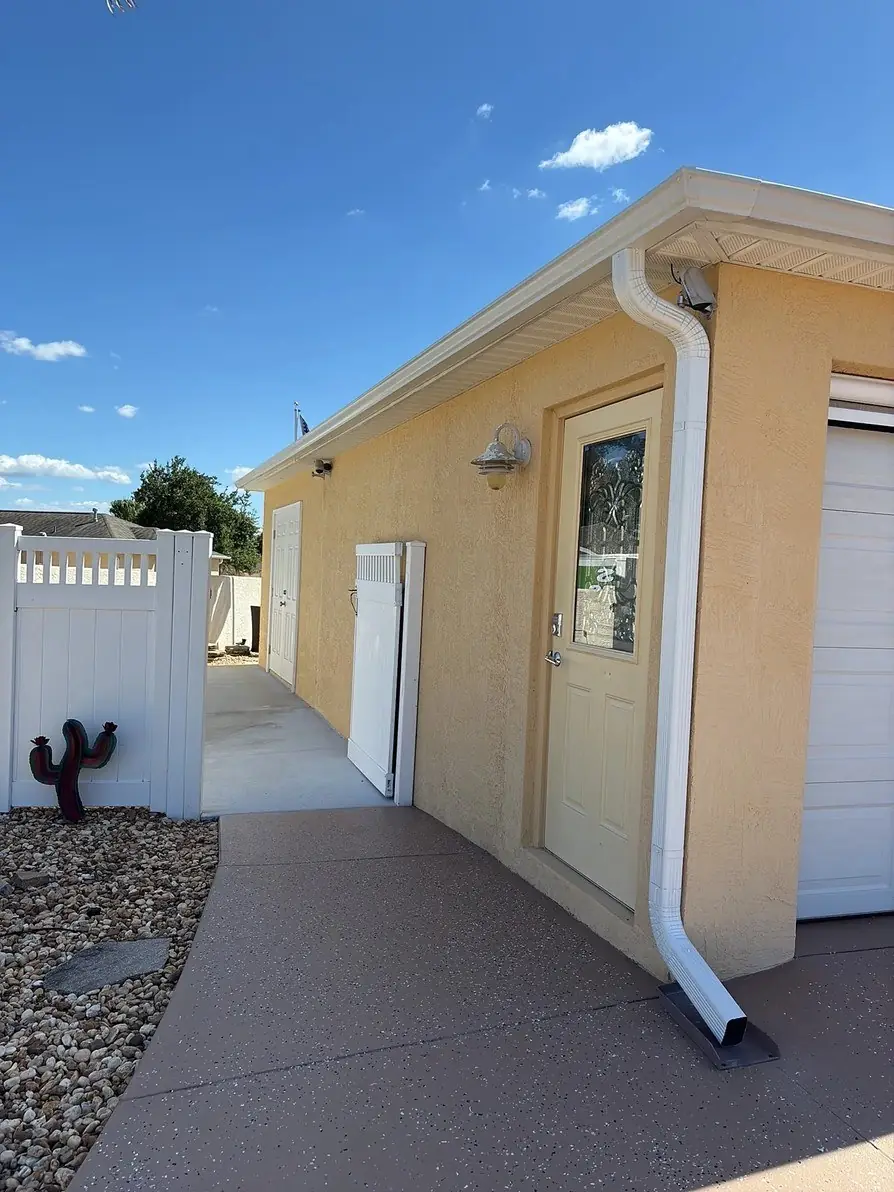 White gutter and downspout on a yellow stucco wall beside a walkway