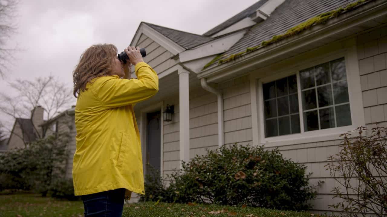 Woman inspecting house gutters with binoculars