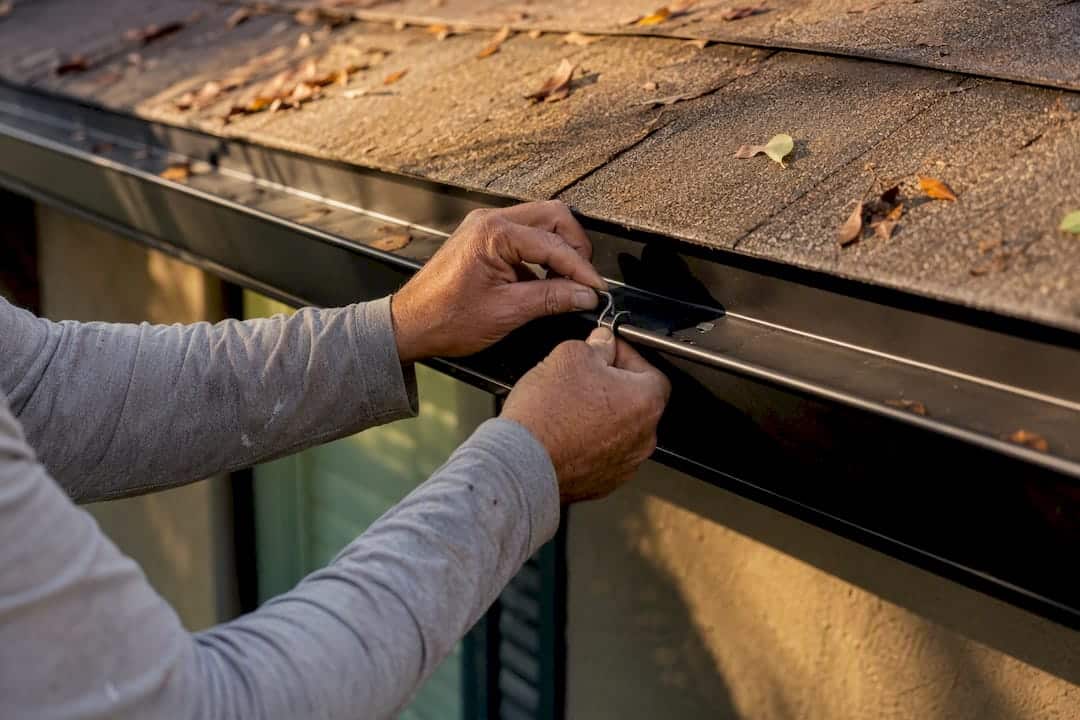 Hands installing gutter hanger without fascia